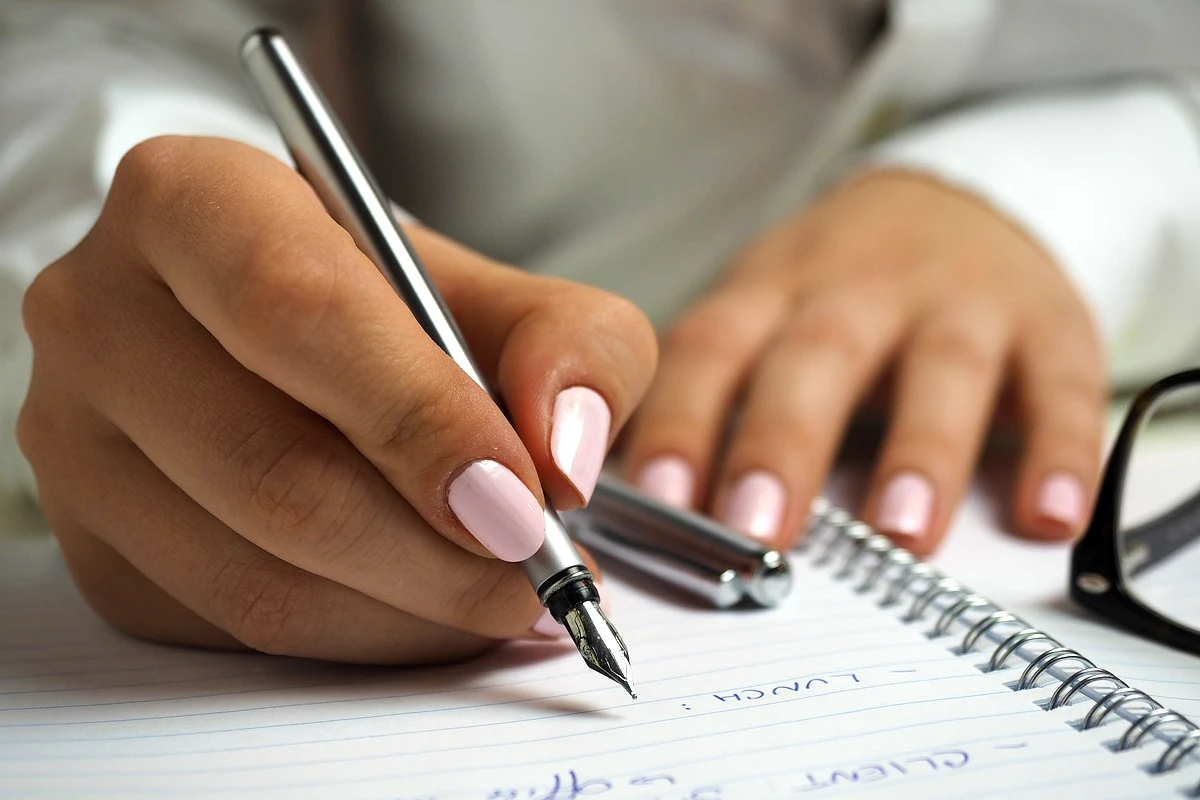 mulher escrevendo com uma caneta em um caderno. Imagem usada para ilustrar o que é acentuação gráfica